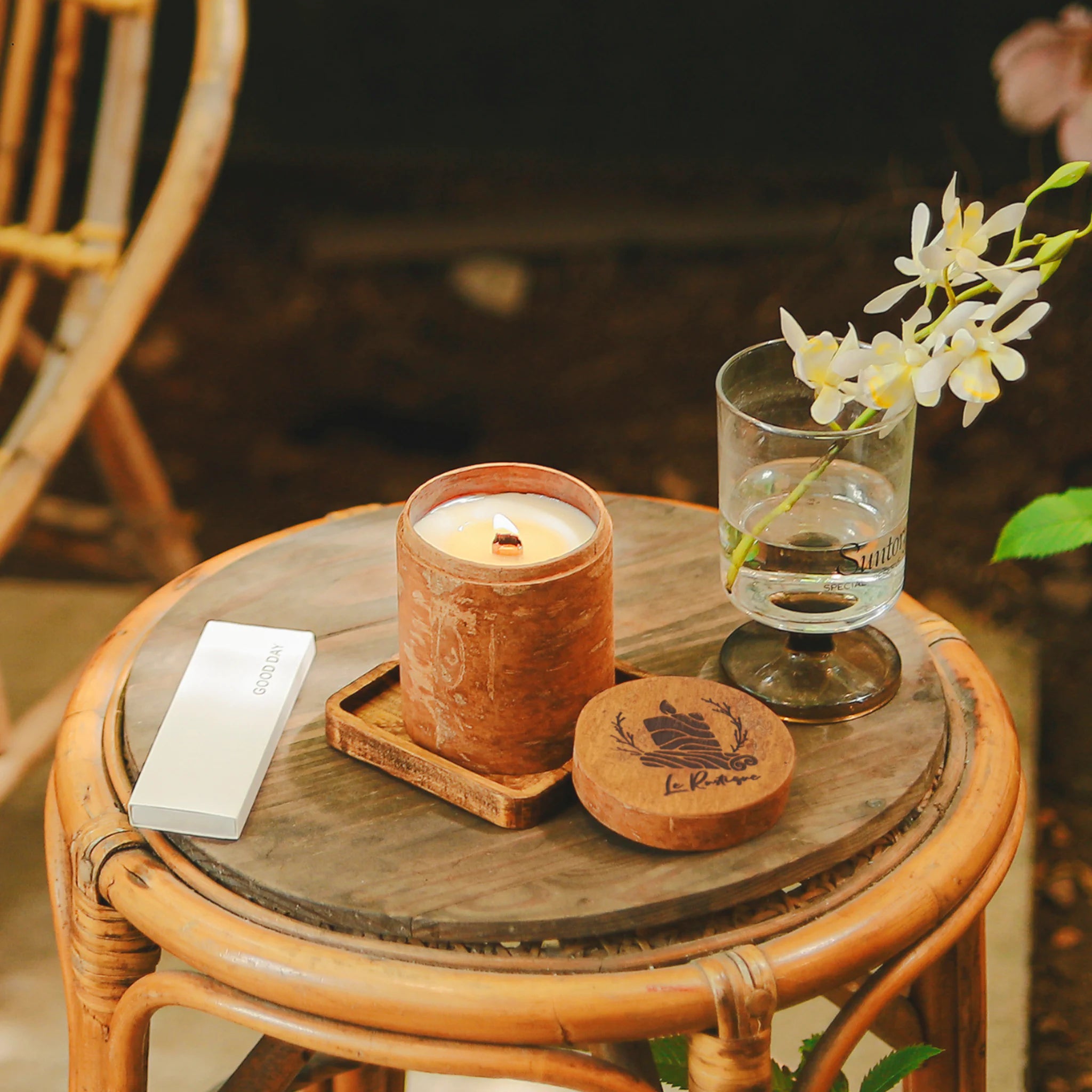 natural scented candle, glass with water, and coaster on a wooden table outdoors